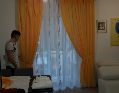 Room with yellow curtains, a white curtain, and a person standing near the window.